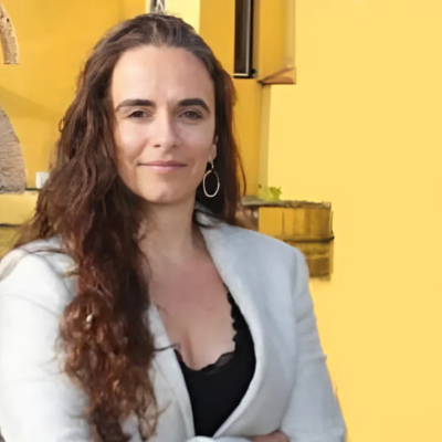 Headshot of Carla Silva, AI Specialist, looking at the camera in front of a yellow building.